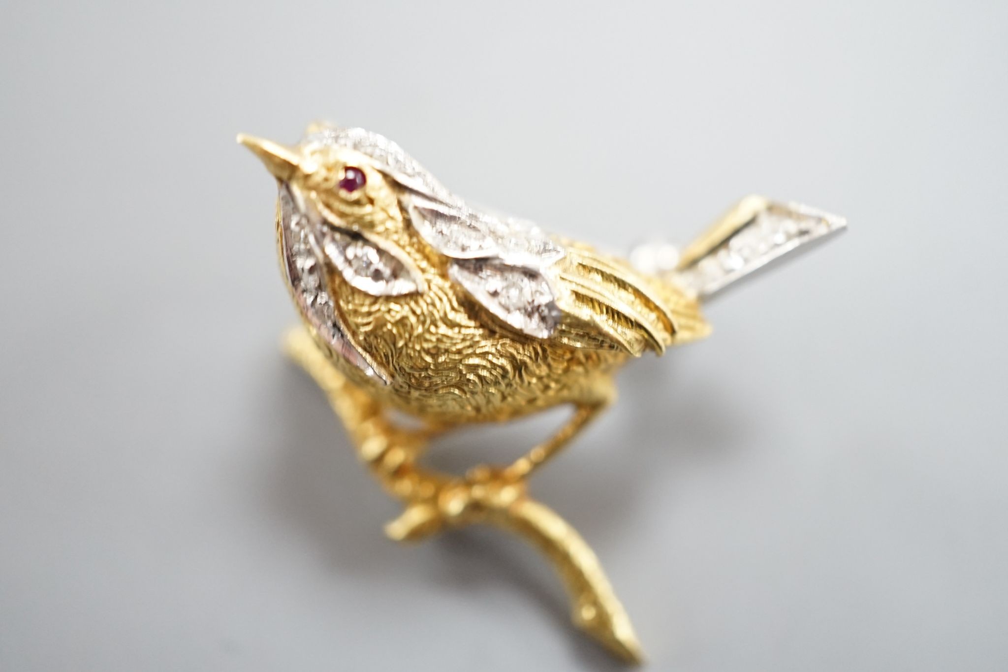 A modern textured 18ct two colour gold, ruby and diamond set bird brooch, 24mm, gross weight 6 grams.